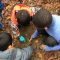 Three small children crouch to inspect an item in the muddy earth